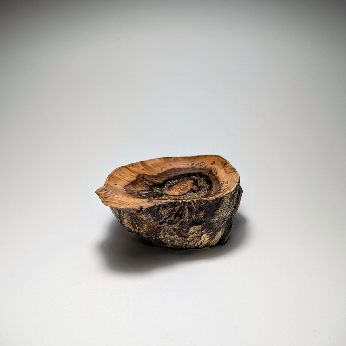 A small rustic wooden bowl or dish made from a natural wood slice with visible grain and bark, photographed on a clean light gray to white studio background.